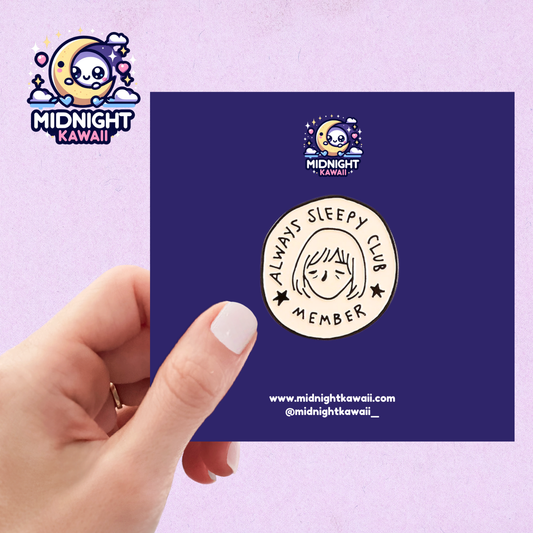 A white circular enamel pin with a pencil style drawn tired face in the centre in black, with the words "ALWAYS SLEEPY CLUB MEMBER" engraved in black around the perimeter of the pin. Size 3-4cm. The pin has a securing arrangement on the back to enable attachment to clothes, bags etc.