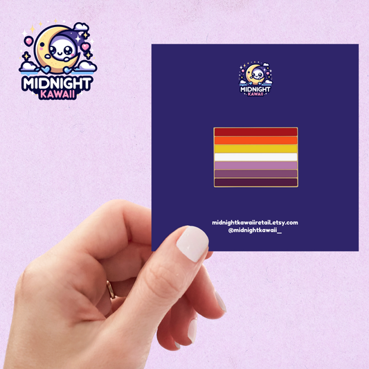 Hand holding a navy card with an enamel pin that showcases a lesbian pride flag