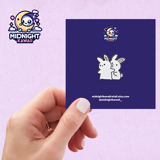 Enamel pin with two white chibi cute bunnies. One of the bunnies is trying to kiss the other, but the other bunny is refusing and facing the other direction. Size 3-4cm. The pin has a securing arrangement on the back to enable attachment to clothes, bags etc.